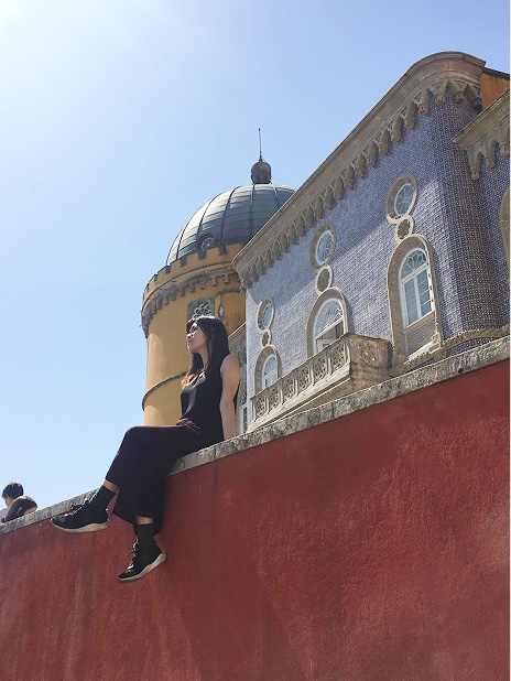 Nicole sitting on a red wall in front of a tiled palace
